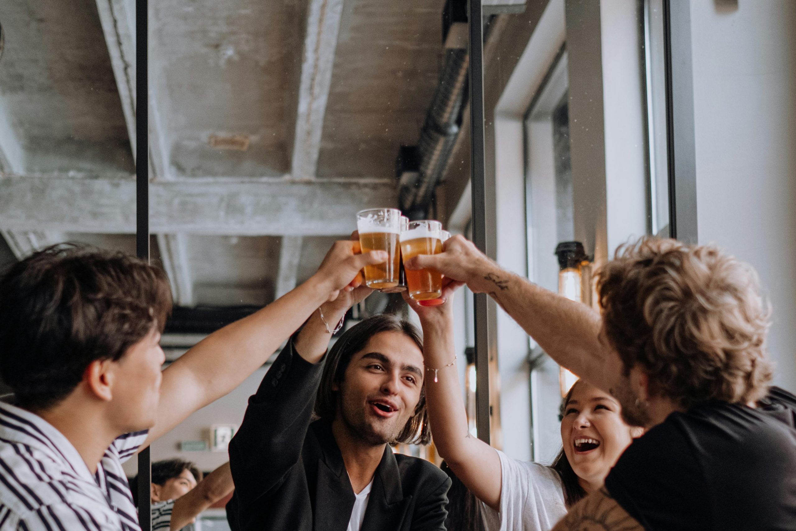 Four friends at a bar, cheersing with their beer. 