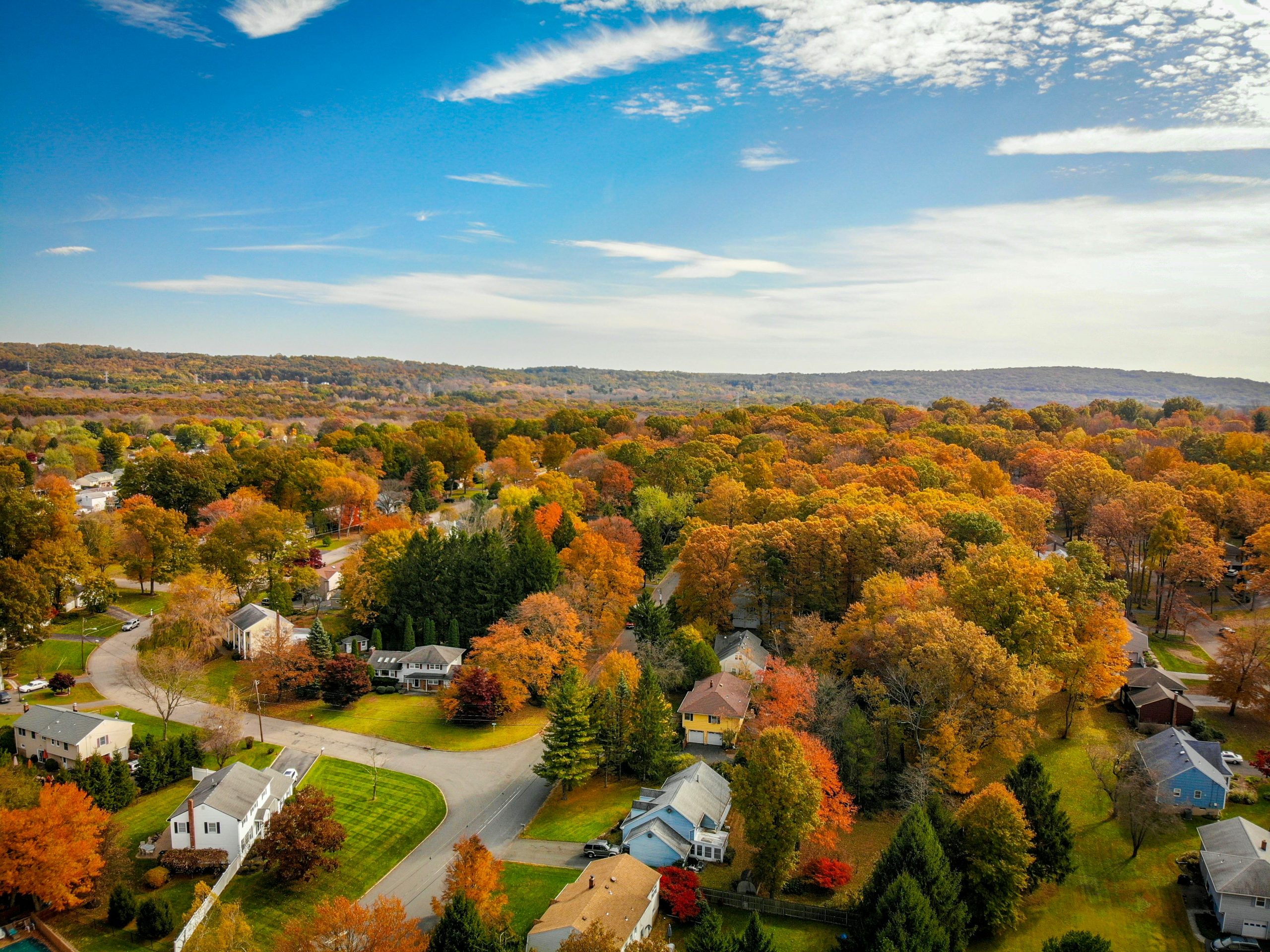 Aerial view of a neighborhood surrounded by trees with vibrant fall foliage.