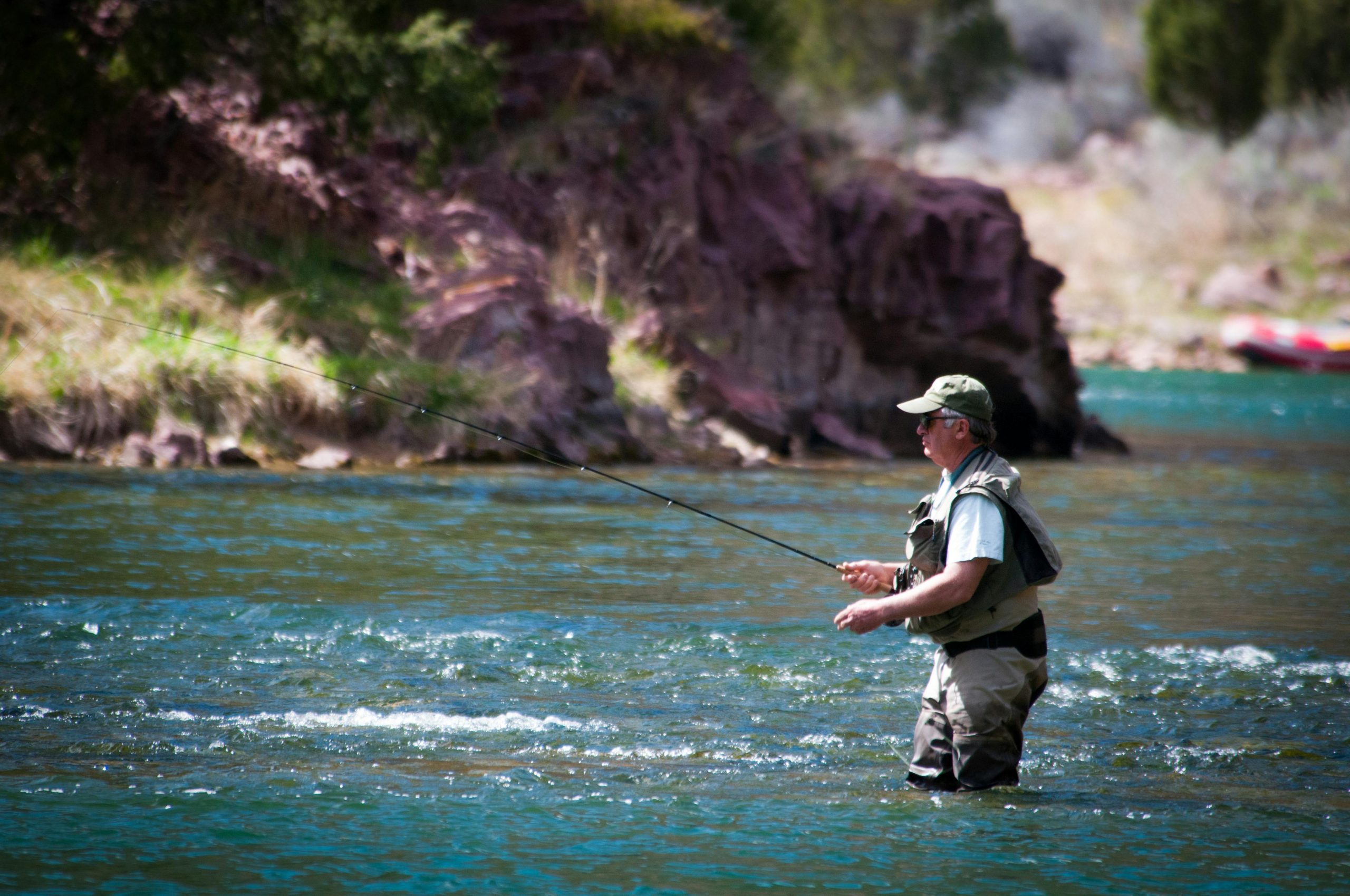  A man standing in a river, fishing in a mountain setting. 