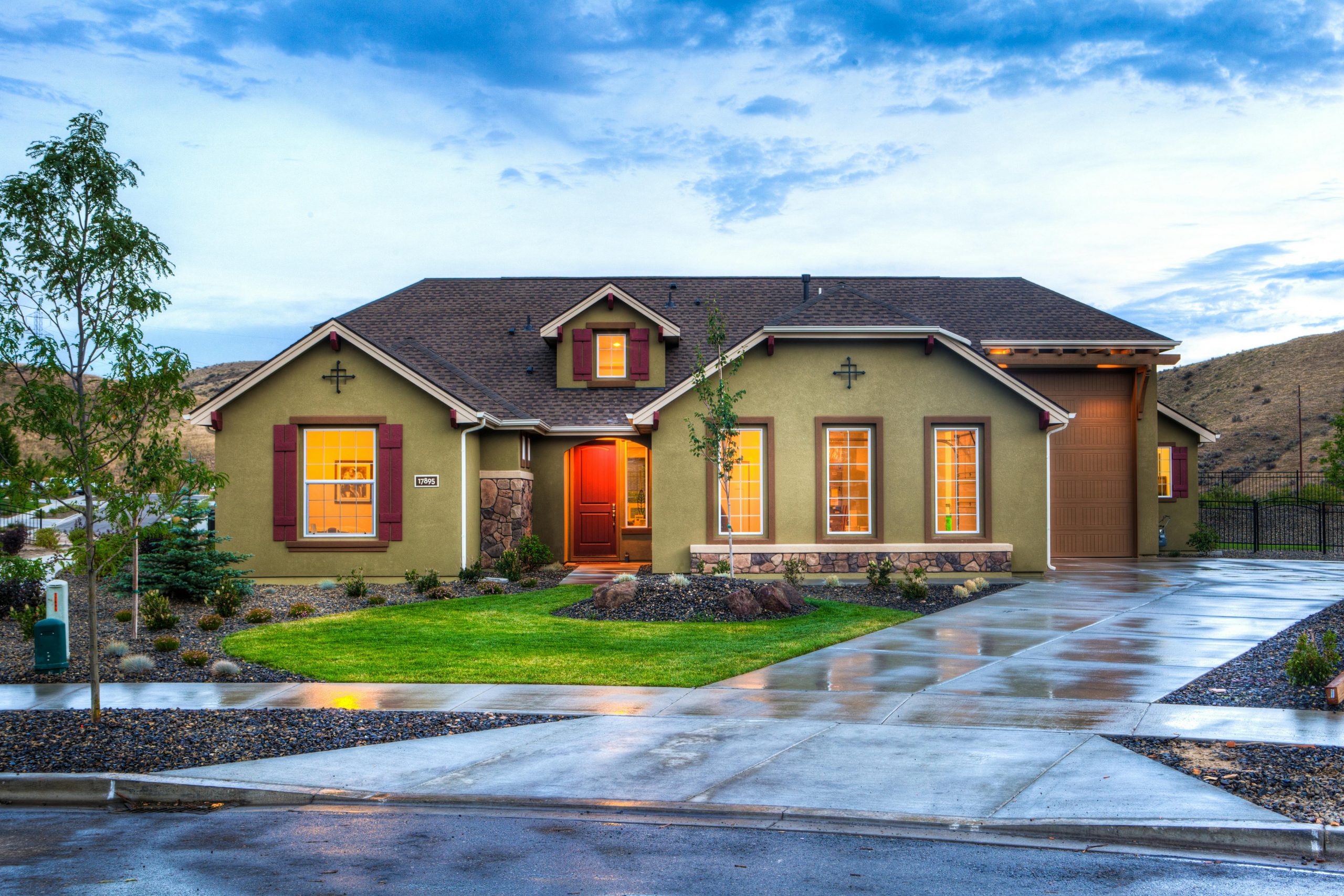 A green home sits nestled in rolling hills, warmly lit in the evening glow.