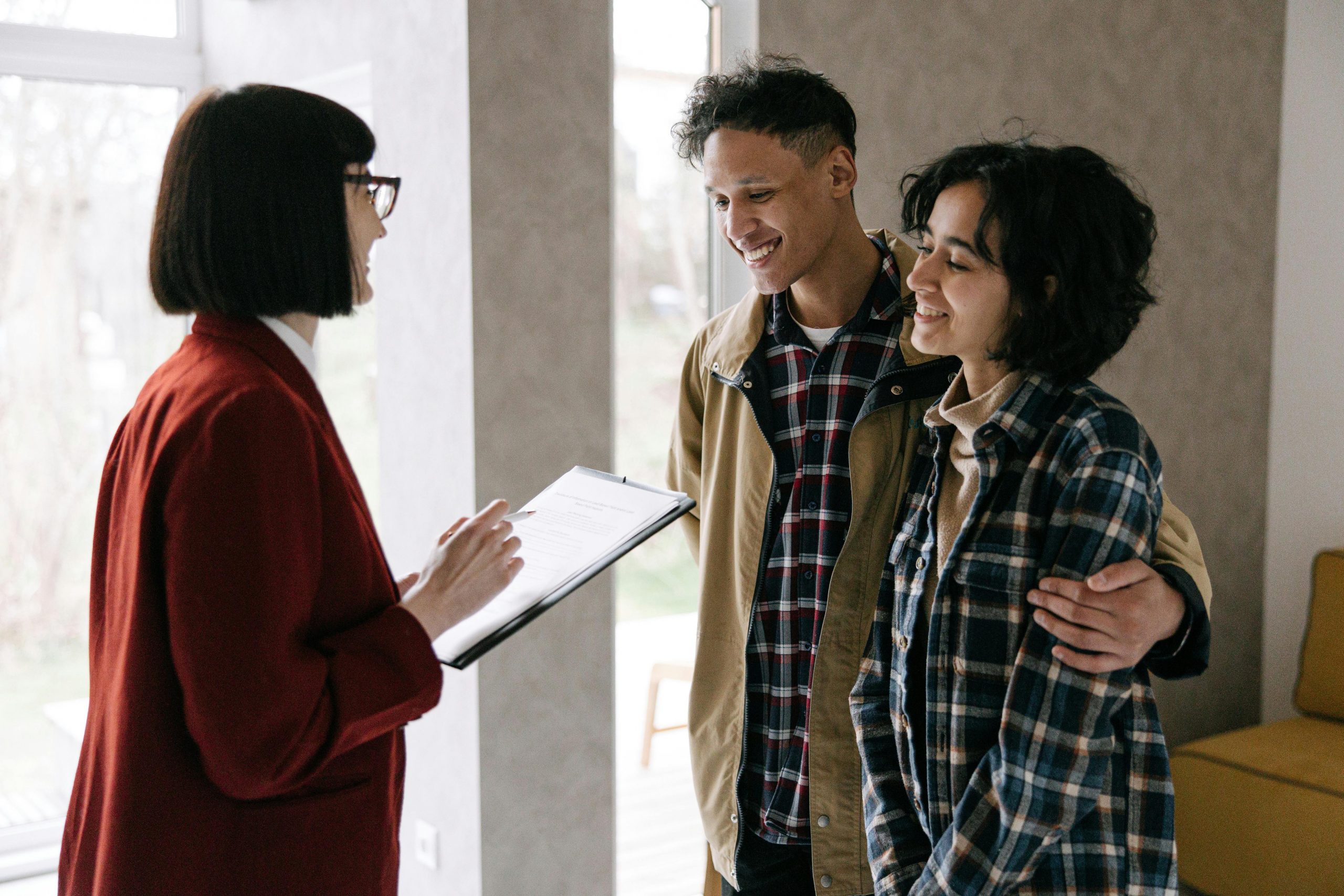 Man and woman stand together in a couple listening as a real estate agent talks to them about the home-buying process. 